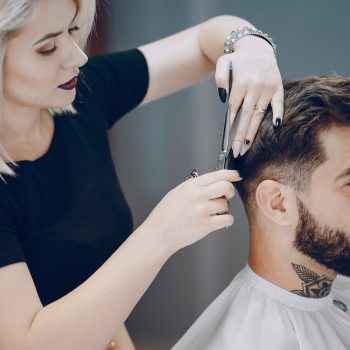 handsome young bearded guy sitting in an armchair in a beauty salon and the girl near him cuts his hair